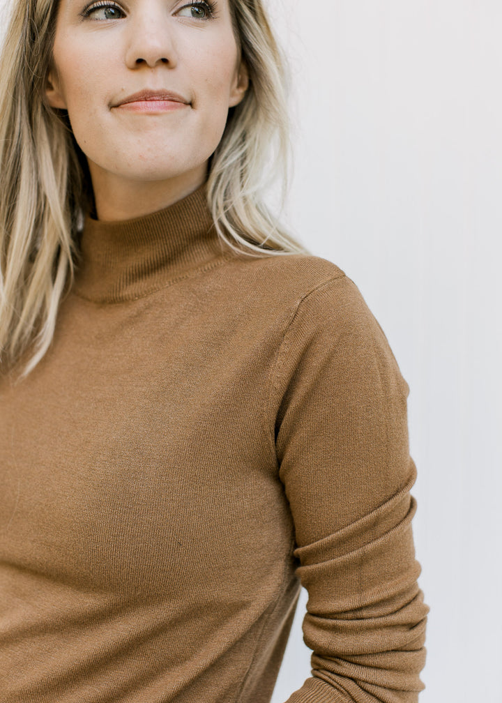Close up view of Model wearing a lightweight caramel knit top with long sleeves and a mock neck. 