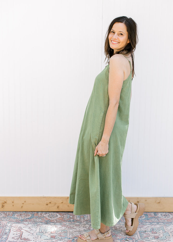Side view of a model wearing a green midi with a v-neck,  adjustable spaghetti straps and pockets.