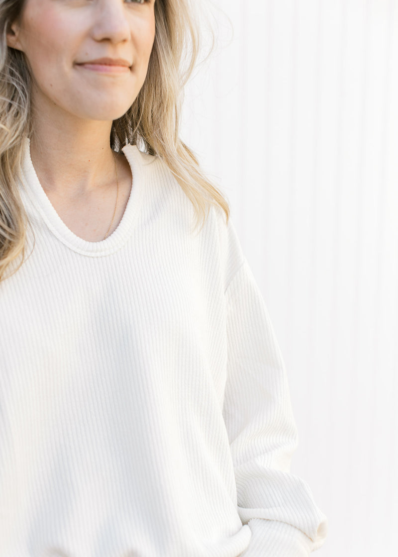 Close up of ribbed material and v-neck on a cream top with exposed hem.