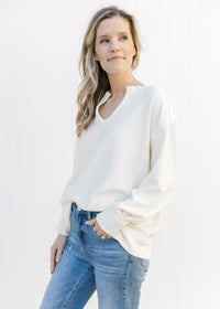 Model wearing jeans with a cream v-neck top with a ribbed material, exposed hem and long sleeves.