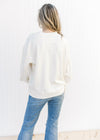 Back view of Model wearing a cream v-neck top with a ribbed material, exposed hem and long sleeves.