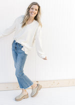 Model wearing jeans, mules and a cream top with a ribbed material, exposed hem and long sleeves.
