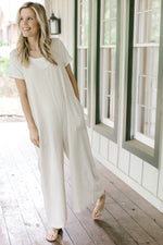 Model waering a sand colored sleeveless jumpsuit with patch pockets and wide legs.