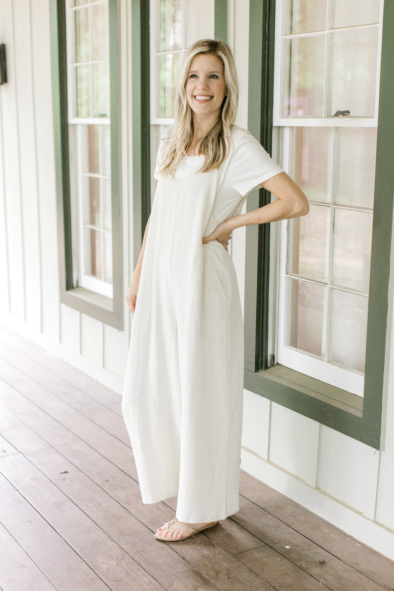 Model wearing a white shirt with a sand colored jumpsuit with patch pockets and wide legs.