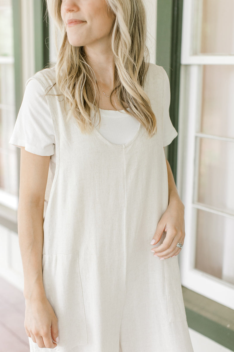 Close up of Model wearing a sand colored jumpsuit with patch pockets and wide legs.