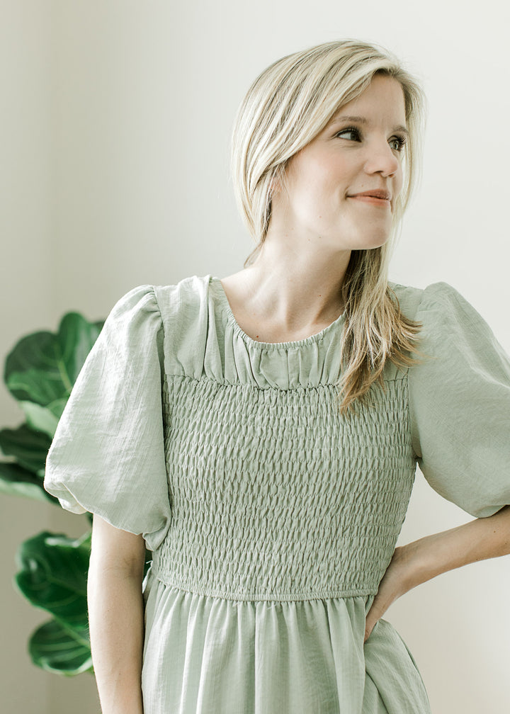 Close up of pleated yolk and smocked bodice on a soft sage short sleeve knee length dress.