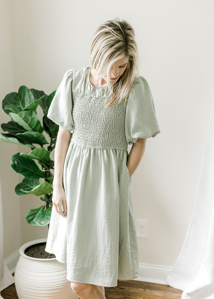 Model wearing a soft sage dress with a bubble short sleeves, smocked bodice and pockets. 