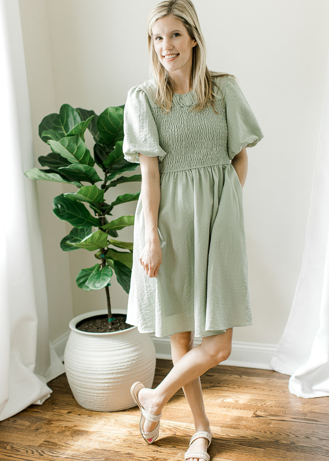 Model wearing sandals and a soft sage dress with a round neck, smocked bodice and short sleeves.
