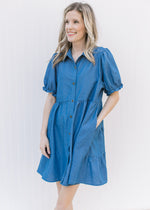 Model wearing a blue button up above the knee dress with bubble short sleeves and pockets.