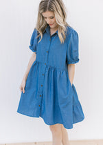 Model wearing a blue button up above the knee dress with bubble short sleeves and a collar.