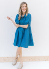 Model wearing mules with a blue button up above the knee dress with bubble short sleeves.