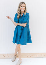 Model wearing mules with a blue button up above the knee dress with bubble short sleeves.