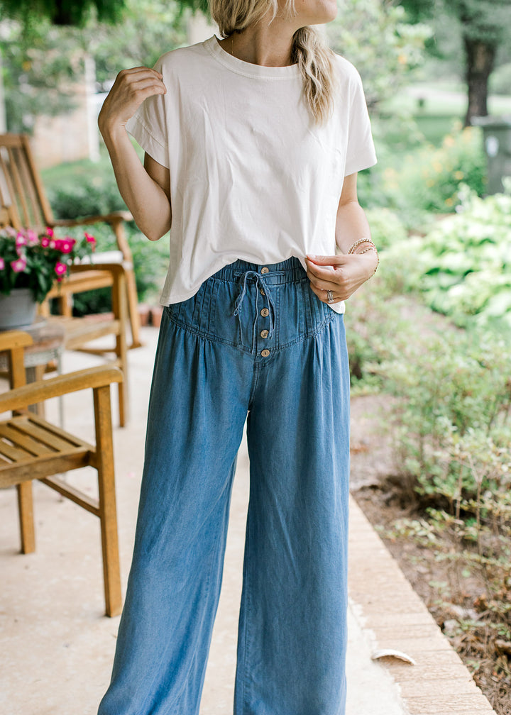 Model wearing white top and chambray wide leg pants with stitched down pleating and button front.