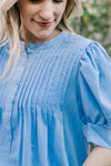 Close up of buttons and micro pleats at the bodice of a soft blue short sleeve blouse. 