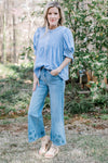 Model wearing jeans and a soft blue woven top with micro pleats at the bodice and short sleeves.