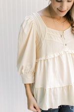 Close up of square neck and three buttons on a cream babydoll top with 3/4 bubble sleeves. 