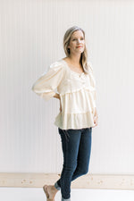 Model wearing jeans with a cream babydoll top with a square neck, 3/4 sleeves and a raw hemline.