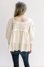 Back view of Model wearing a cream babydoll top with a square neck, 3/4 sleeves and a raw hemline.