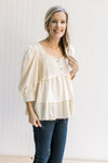 Model wearing a cotton, cream babydoll top with a square neck, 3/4 sleeves and a raw hemline.