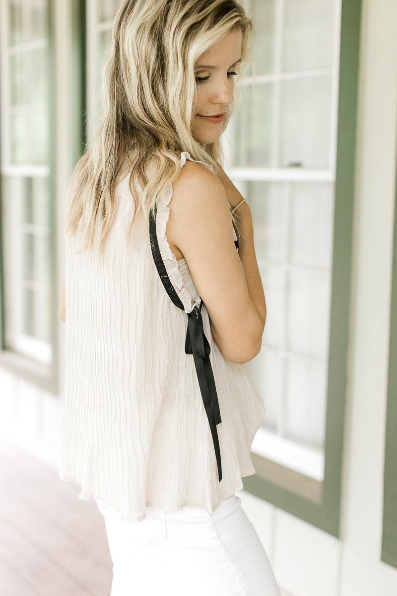 Side view of black bow accent at the base of the sleeveless champagne top.