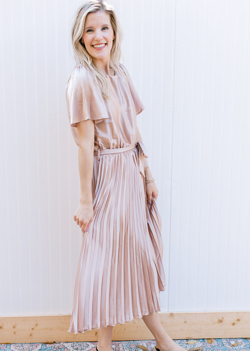 Model wearing a champagne midi with a pleated skirt, tie at the waist and short sleeves. 