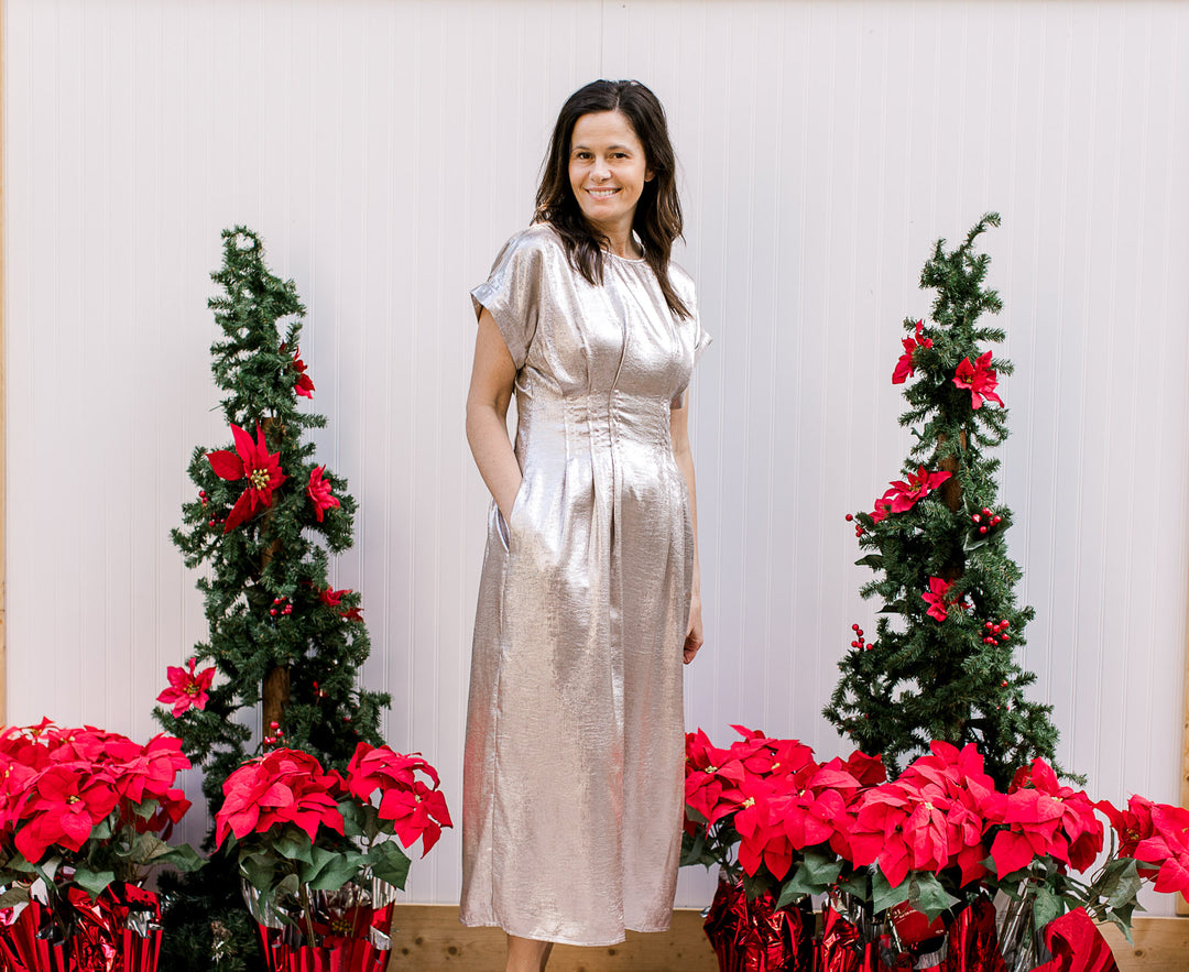 Model wearing a metallic champagne midi with a pleated waist, pockets and short cuffed sleeves.