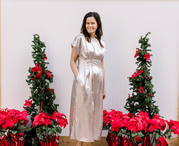 Model wearing a metallic champagne midi with a pleated waist, pockets and short cuffed sleeves.