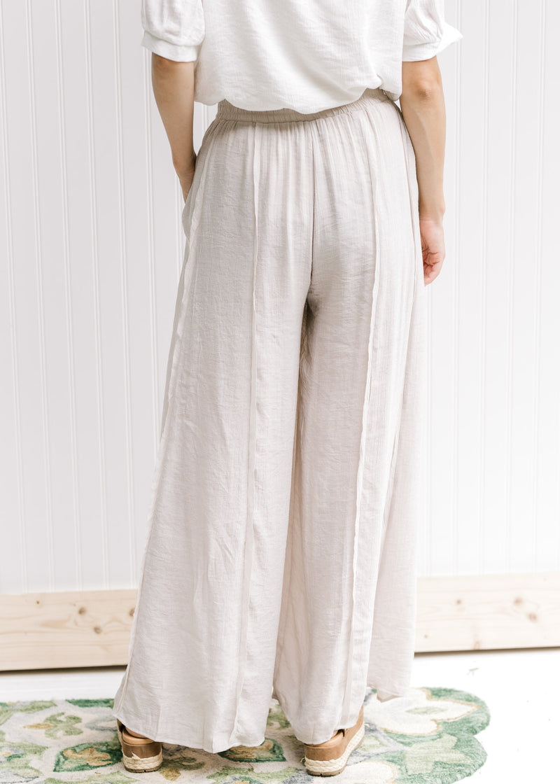 Back view of Model wearing champagne wide leg pants with an elastic waist and pockets. 