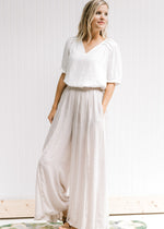 Model wearing a white top with champagne wide leg pants with an elastic waist and pockets. .