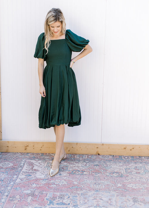 Model wearing a deep green bubble dress with a square neck, bubble short sleeves and pleated waist. 