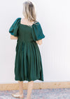 Back view of Model wearing a deep green bubble dress with a square neck and short sleeves.