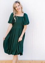 Model wearing a deep green bubble dress with bubble short sleeves and a pleated waist. 