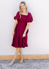 Model wearing gold flats and a deep cranberry dress with bubble short sleeves and hem. 