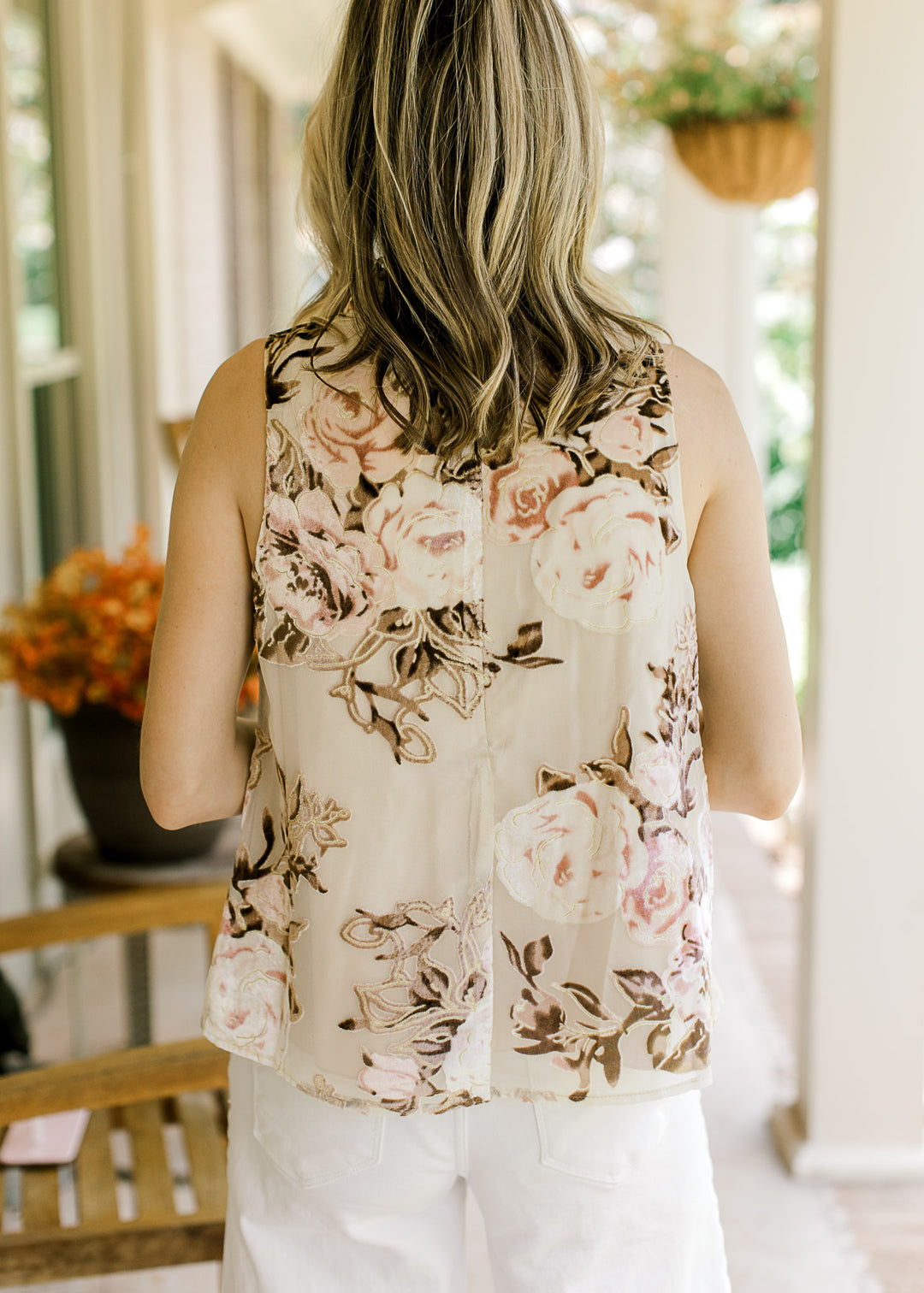 Back view of Model wearing a sleeveless oatmeal top with velvet pink and brown floral and mock neck.
