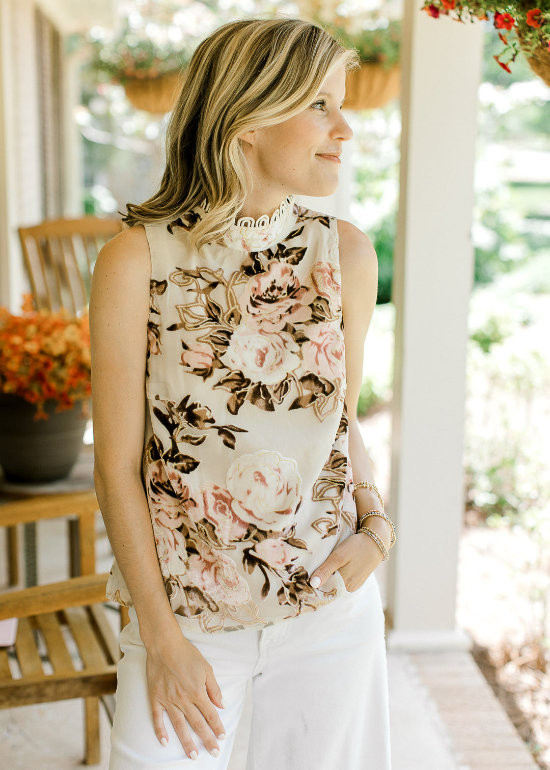 Model wearing white pants and a sleeveless oatmeal top with velvet pink and brown floral.