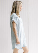 Side view of Model wearing a light blue and cream striped v-neck dress with cuffed short sleeves. 