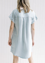 Back view of Model wearing a light blue and cream striped v-neck dress with cuffed short sleeves. 
