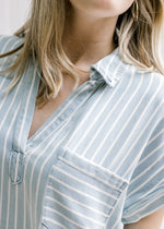 Close up of Model wearing a light blue and cream striped v-neck dress with cuffed short sleeves. 