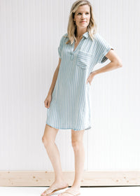 Model wearing a light blue and cream striped v-neck above the knee dress with cuffed short sleeves. 