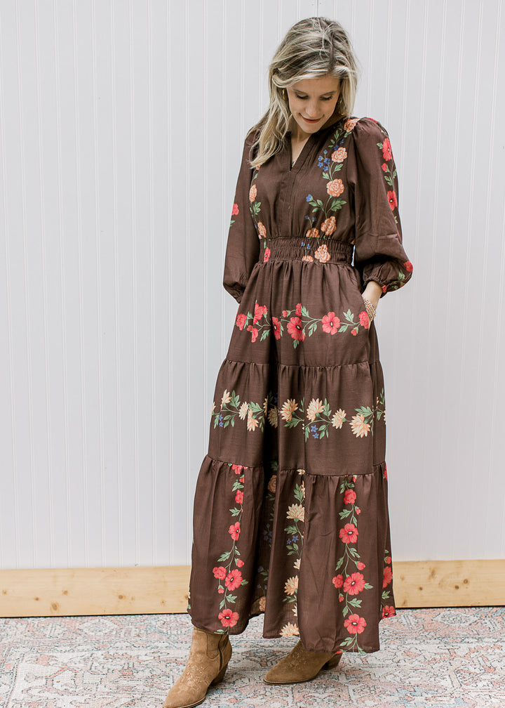 Model wearing a chocolate colored maxi with floral, pockets and 3/4 sleeves with elastic cuffs. 