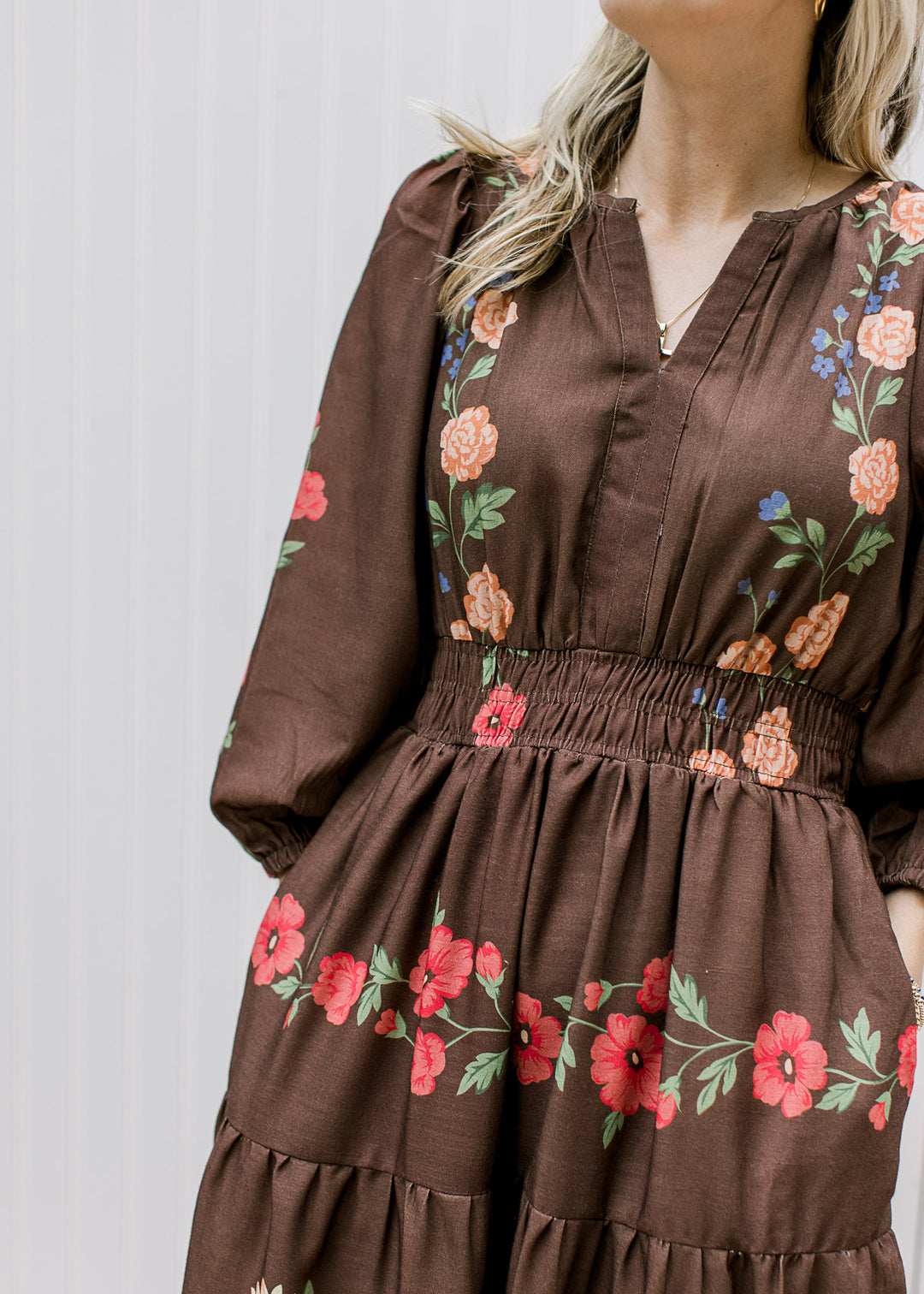 Close up of v-neck, bubble 3/4 sleeves and smocked waistband on a chocolate dress with floral. 