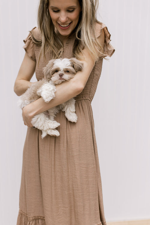 Model holding a puppy, wearing a light brown midi with a smocked bodice and flutter cap sleeves.