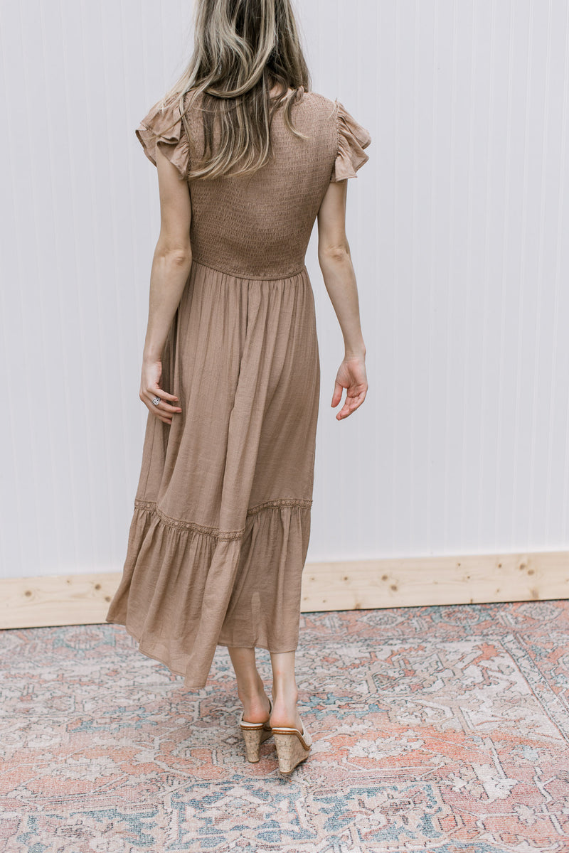 Back view of a model waering a light brown midi with a smocked bodice and ruffle cap sleeves. 