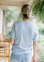 Back view of Model wearing a pale blue tee with floral graphic and words chosen, adopted and loved. 