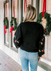 Back view of Model wearing a black sweater with colored sequins lights and long sleeves. 