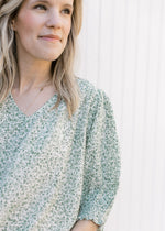 Close up of 3/4 bubble sleeves and v-neck on a cream top with a green floral print. 