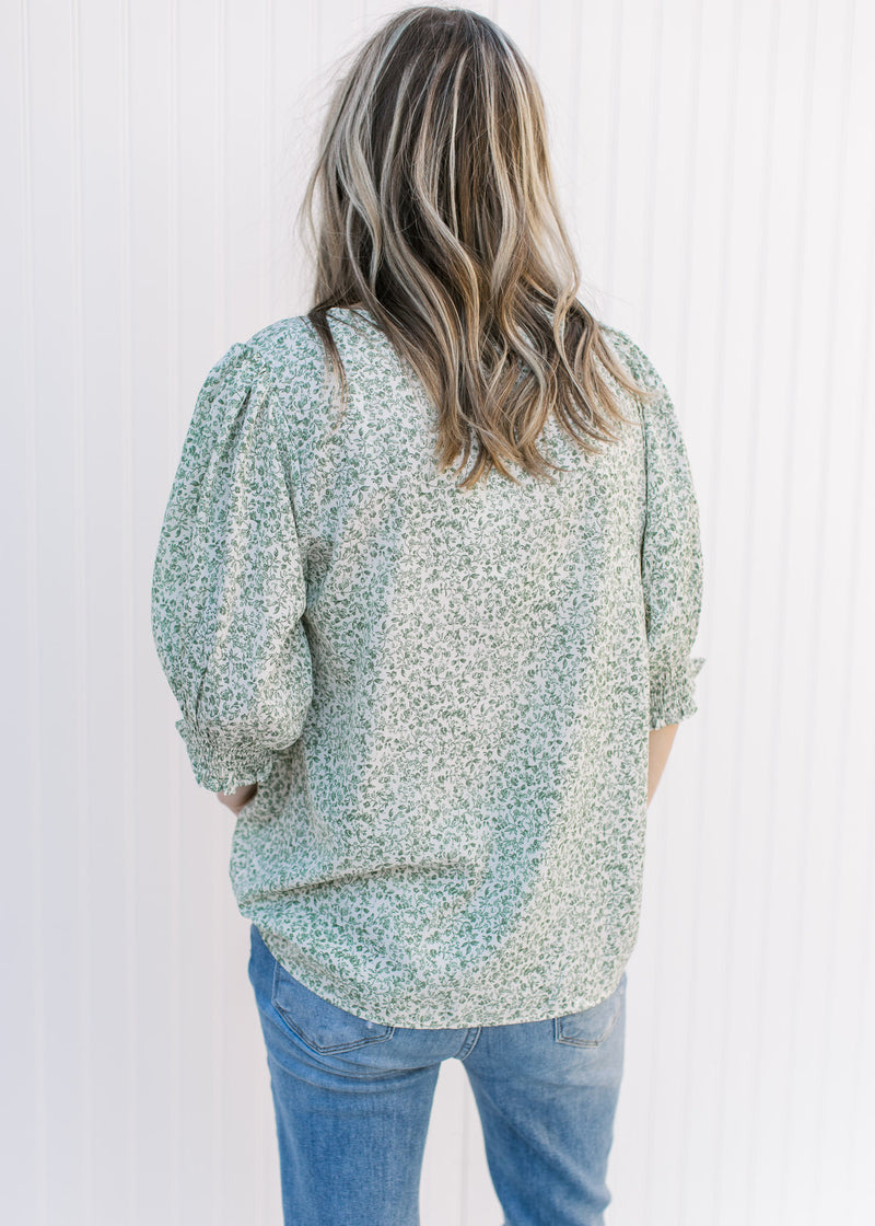 Back view of Model wearing a polyester, cream v-neck top with green floral print and 3/4 sleeves.