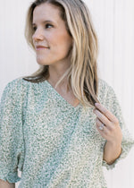 Model wearing a cream polyester top with green floral print and 3/4 bubble sleeves.