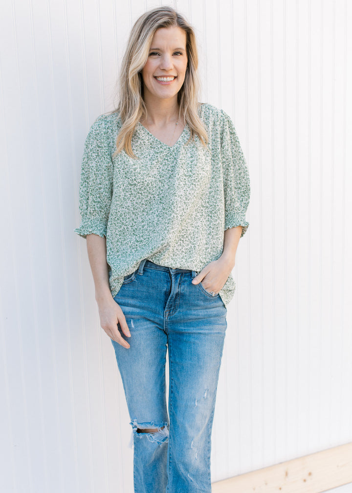 Model wearing a cream top with green floral print, 3/4 bubble sleeves and a polyester material.