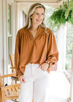 Model wearing a cinnamon blouse with smocked detail at shoulder, poet long sleeves and v-neck.